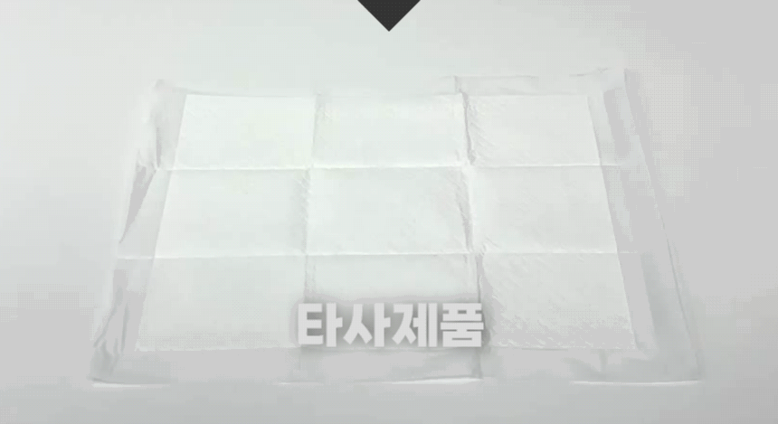 타사 배변패드를 손으로 밀어 바닥에서 움직이는 모습을 보여주는 비교 시연.